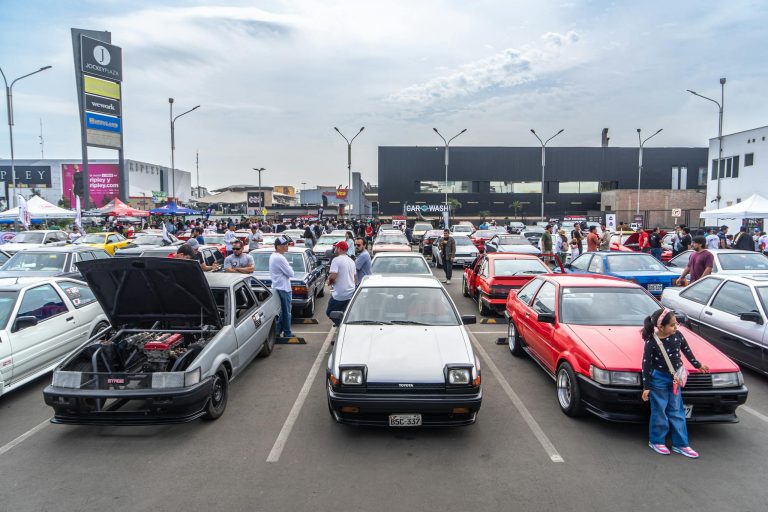 A bustling car event in an outdoor parking lot showcasing classic Toyota cars with a lively crowd.