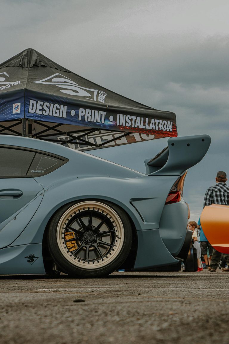 A customized Toyota Supra with body kit and spoiler showcased at an outdoor car event.