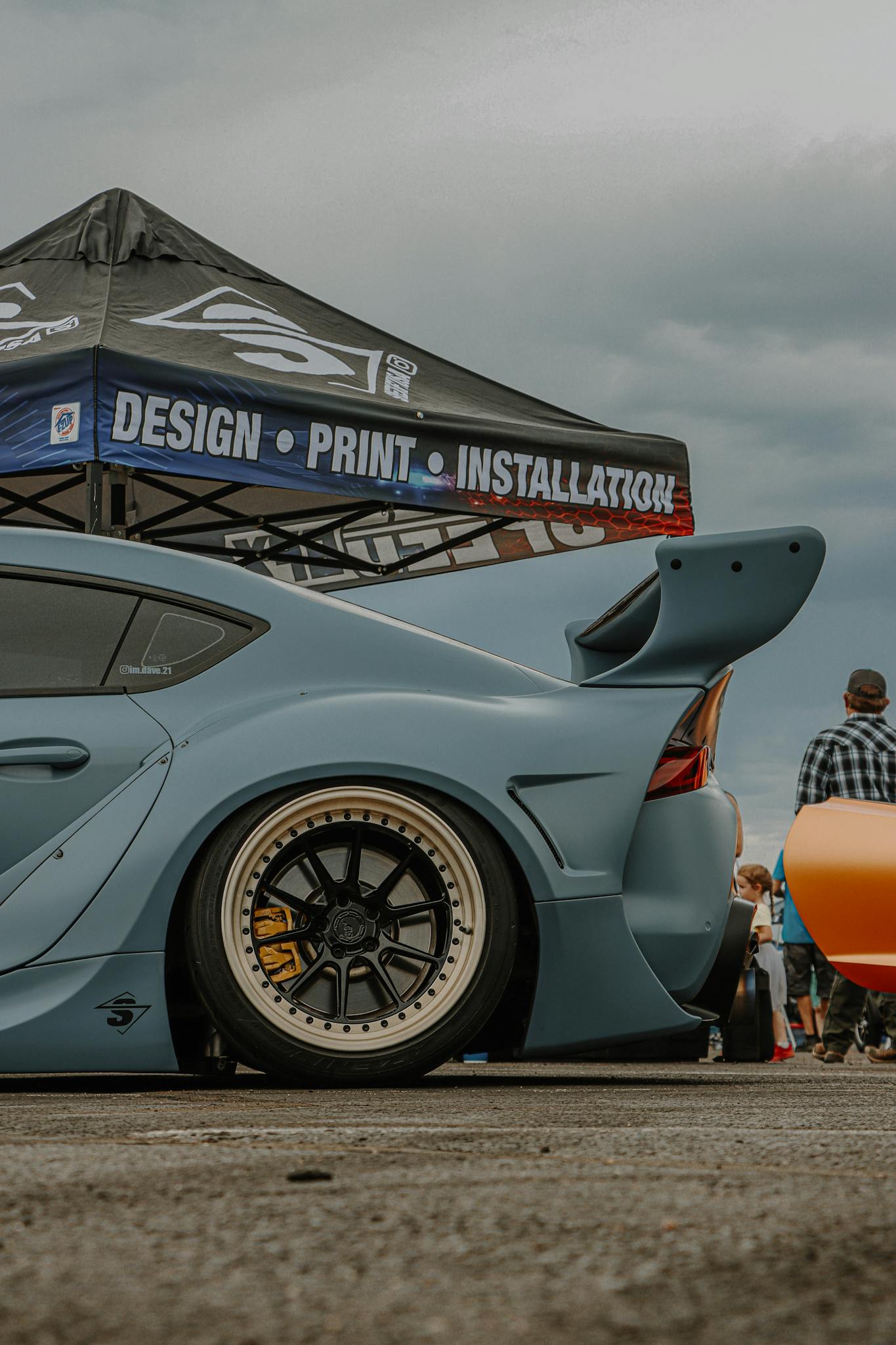 A customized Toyota Supra with body kit and spoiler showcased at an outdoor car event.
