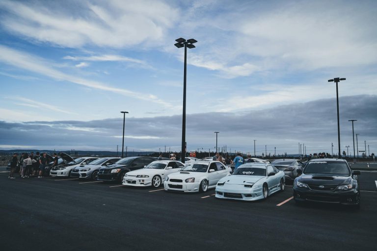 A lineup of sports cars gathered in an open parking lot during the evening, showcasing car culture.